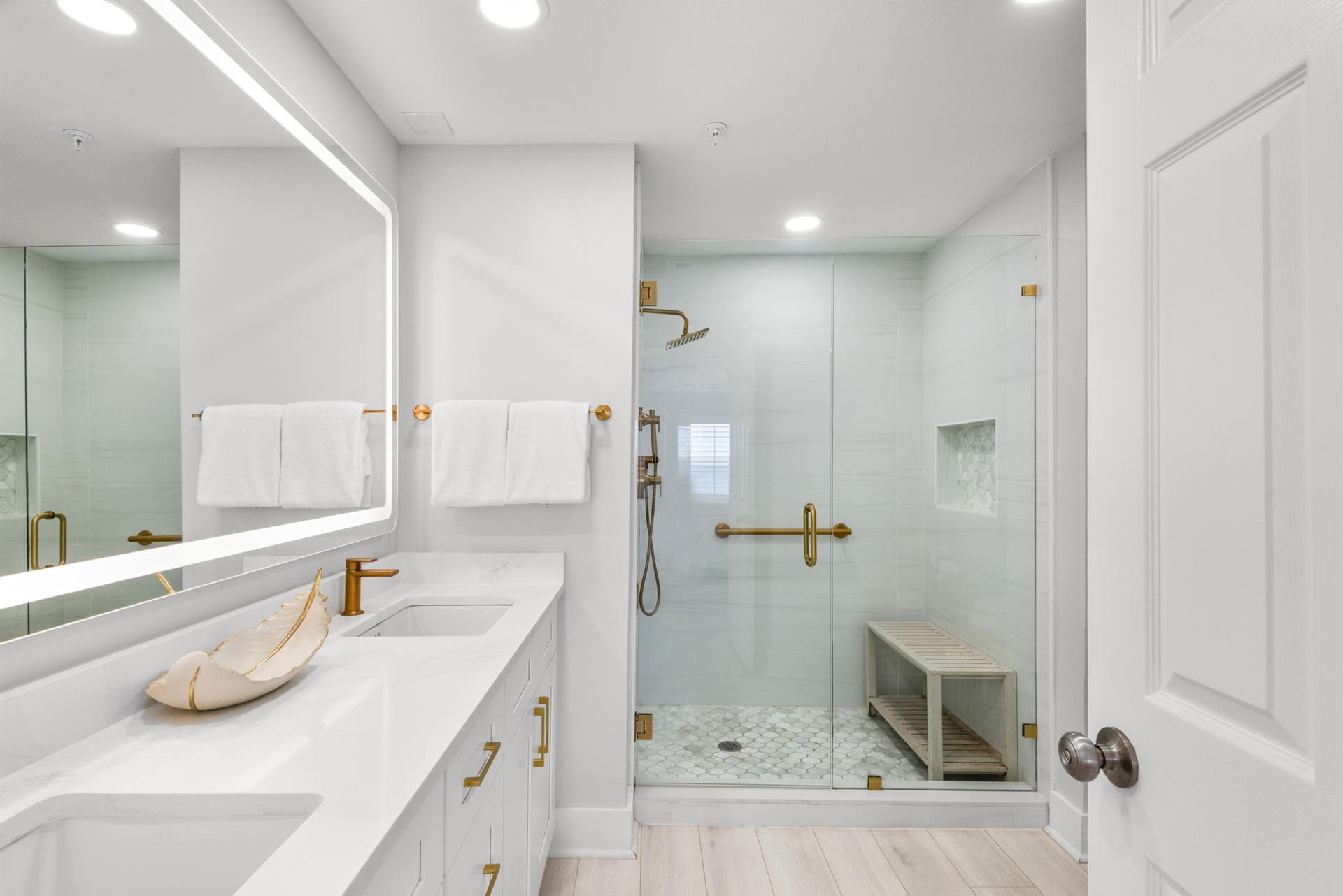 Step into a spalike bathroom with double vanities, bright LED lighting, and a spacious walkin shower featuring elegant gold fixtures and calming tile that invites you to unwind in comfort.