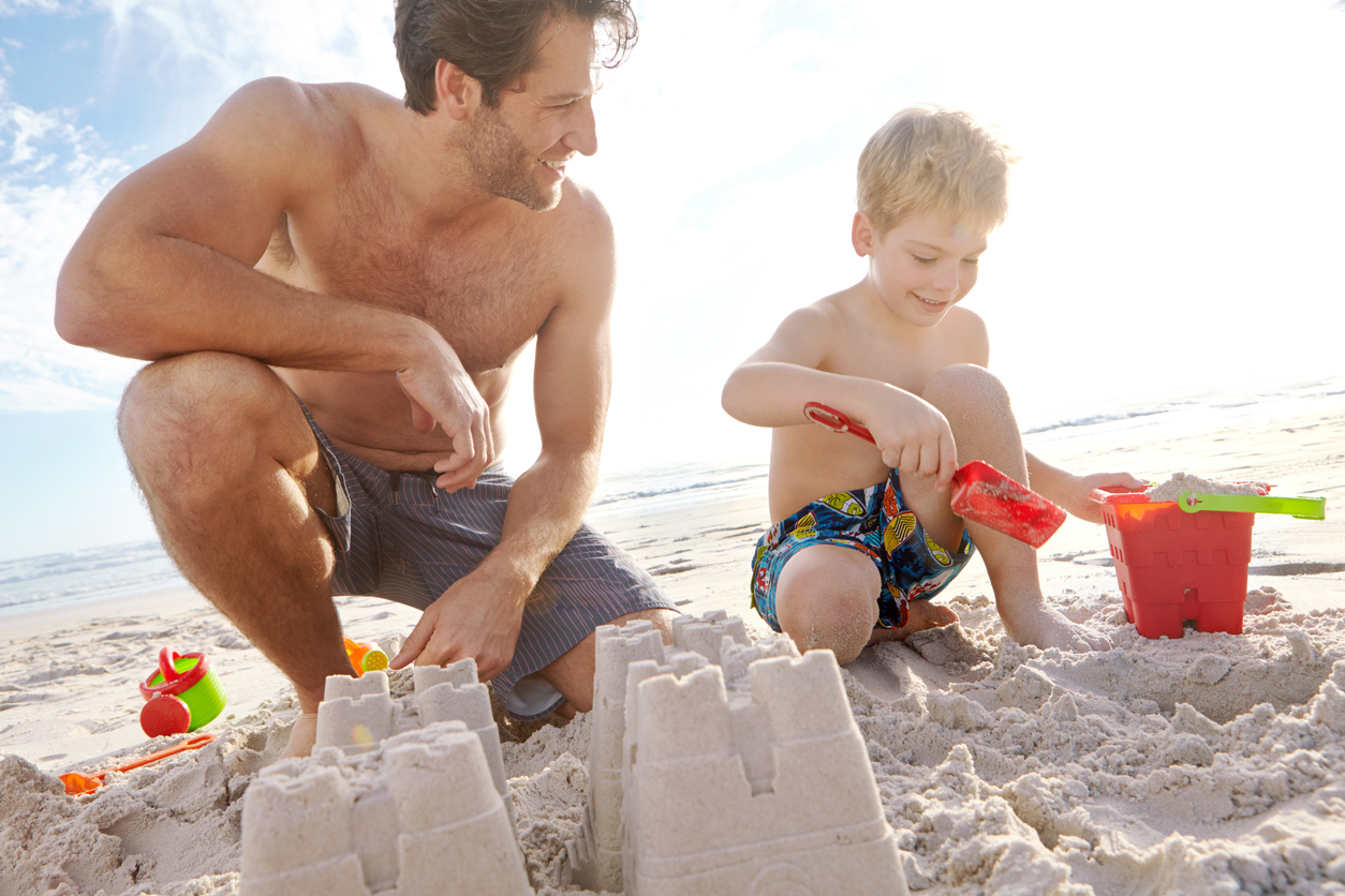 dad showing son how to build a sandcastle at beach