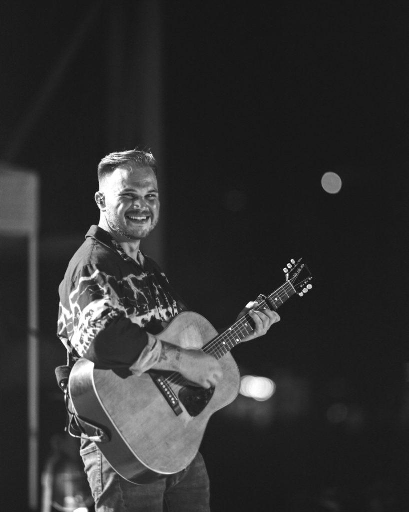 Country Artist Luke Bryan playing guitar and smiling for the camera.