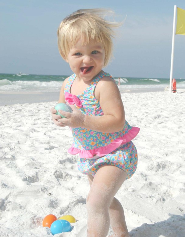 Little Amy is smiling with delight after picking up an Easter egg on the beach.