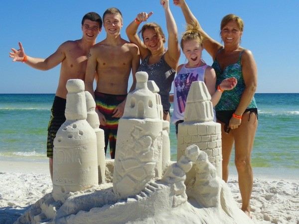 A family poses behind the sandcastle they built on the beach.