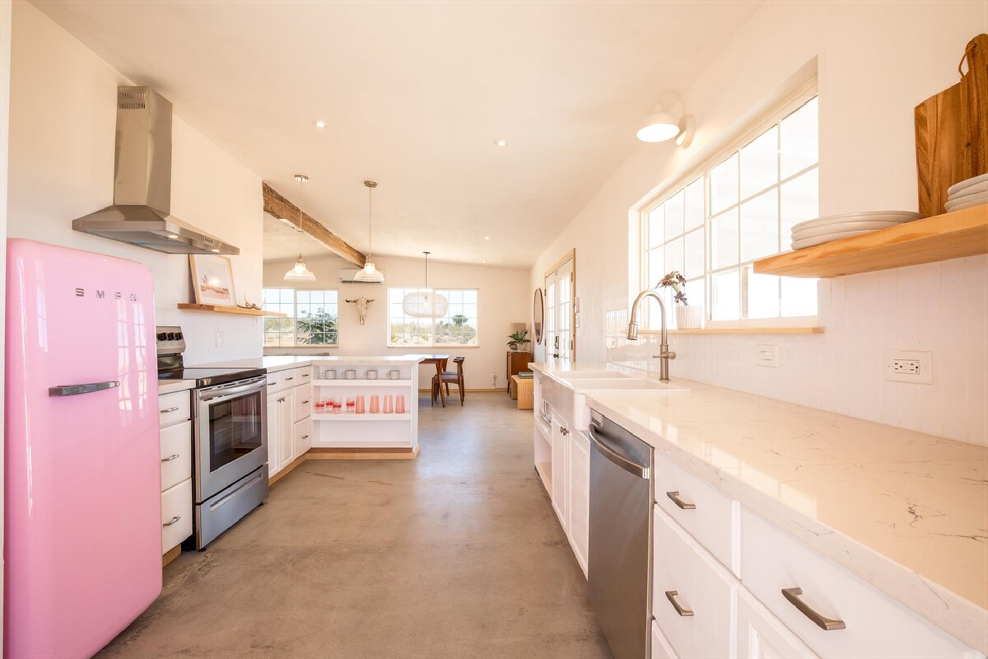 Full kitchen equipped with quartz counters, dishwasher, farmhouse sink, Smeg Refrigerator, and builtin shelving.