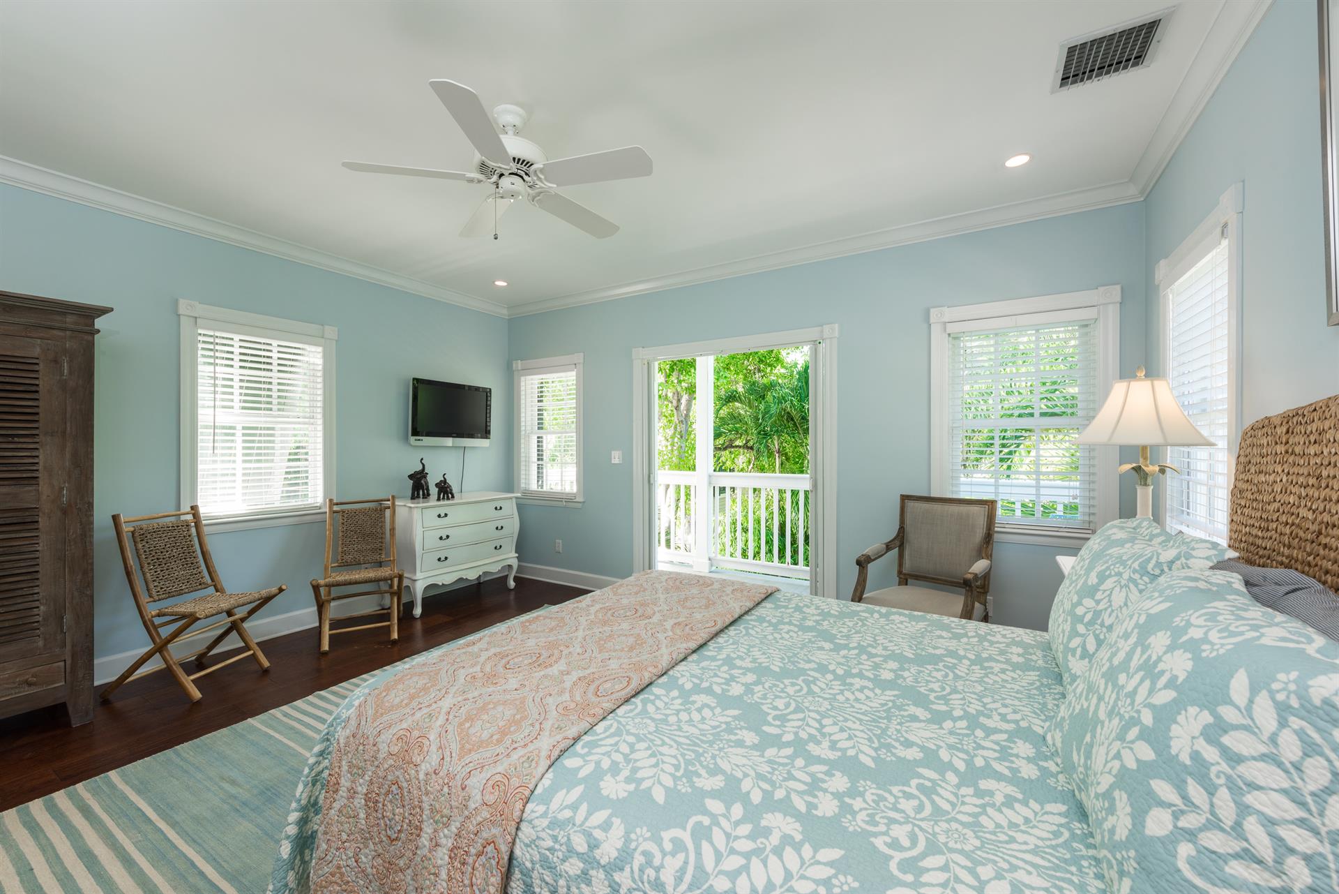 This spacious bedroom has a dresser, TV, and ceiling fan.