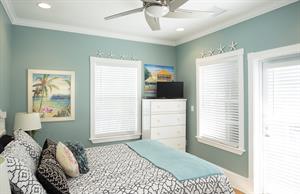 Queen bedroom has dresser, TV, ceiling fan, and balcony access.