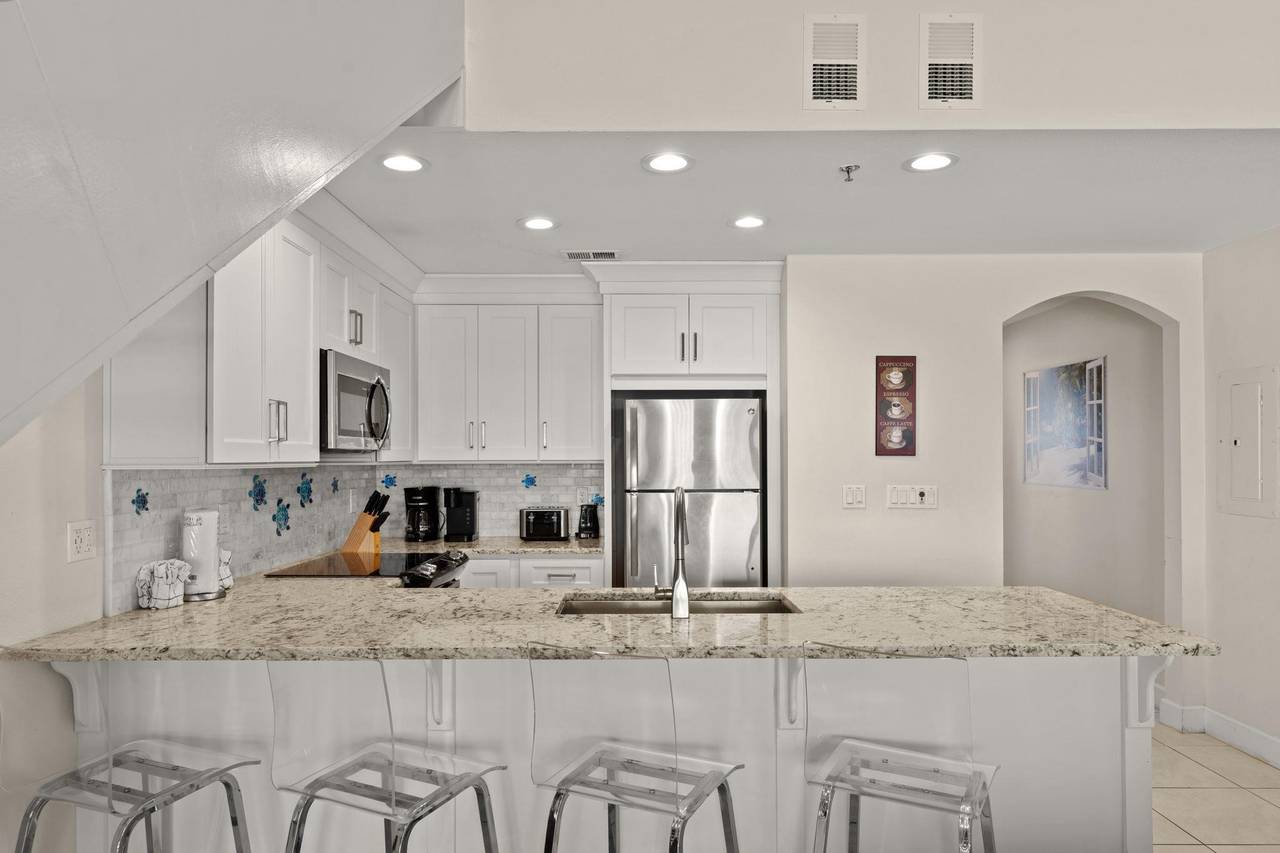 Step into your bright, modern kitchen with granite countertops, sleek white cabinetry, and a welcoming breakfast bar where you can enjoy your morning coffee.