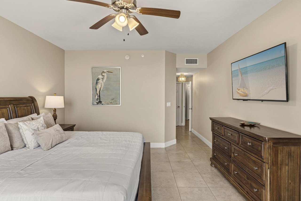 Unwind in your serene bedroom with plush bedding, coastal artwork, and a gentle ceiling fan keeping you cool during peaceful nights.