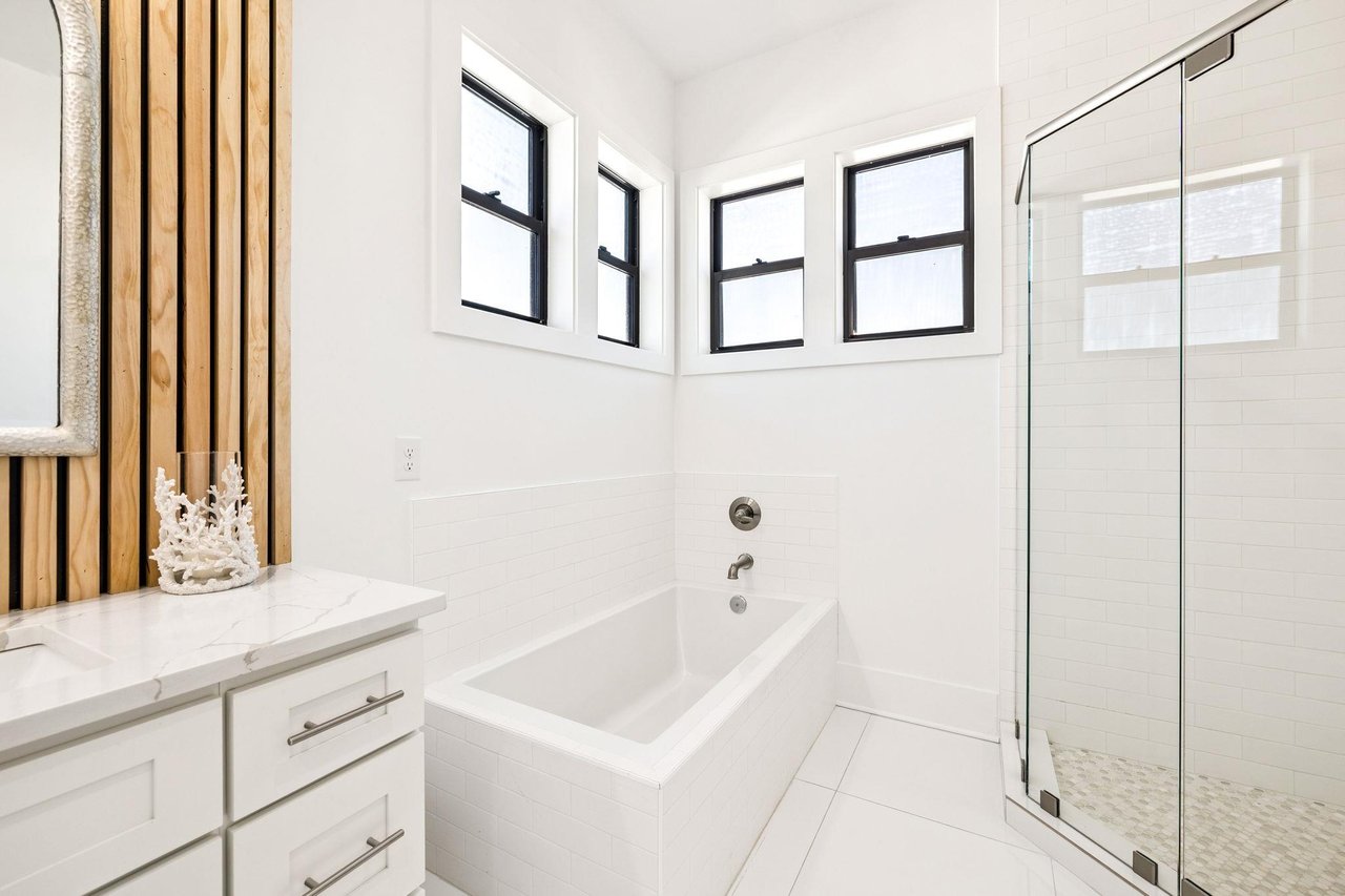Unwind in your bright, modern bathroom featuring a deep soaking tub and glassenclosed shower beneath windows that bathe the space in natural light.