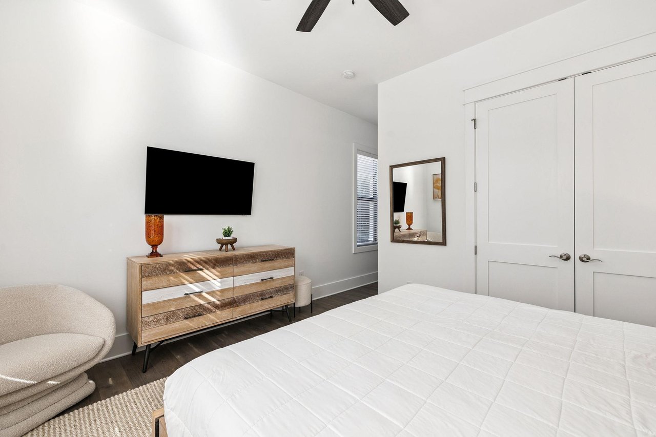 Unwind in your serene bedroom featuring a plush bed, modern TV, and stylish wood dresser beneath soaring ceilings with rustic beams.