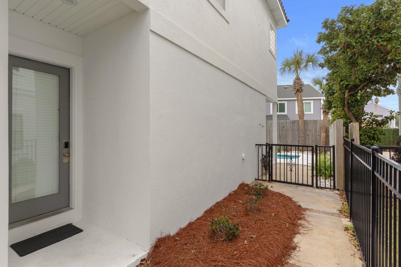 A clean side entrance with fenced pathway leads to the pool area, surrounded by tropical landscaping and neighboring homes.