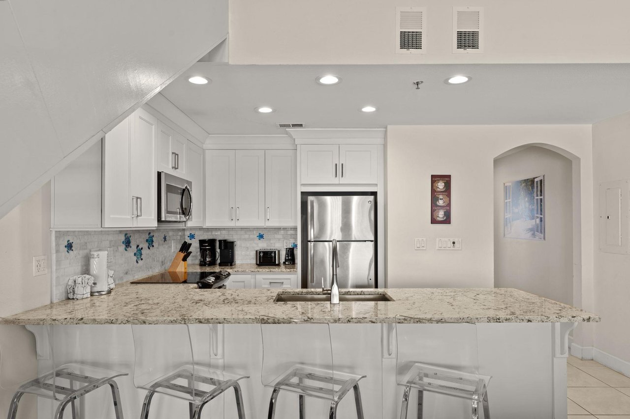 Step into your bright, modern kitchen with granite countertops, sleek white cabinetry, and a welcoming breakfast bar where you can enjoy your morning coffee.