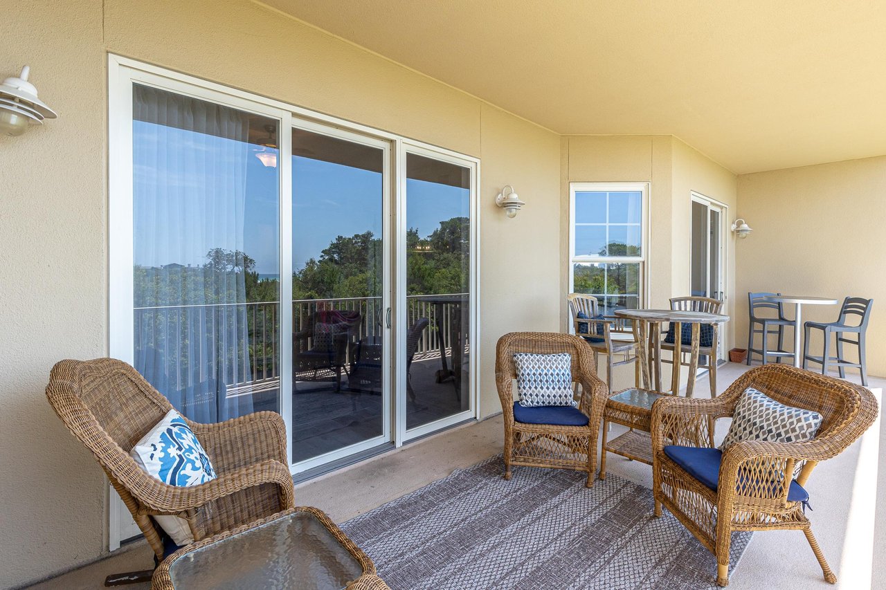 Covered balcony provides a comfortable retreat with wicker seating, bistro table, and peaceful treetop views stretching into the distance.
