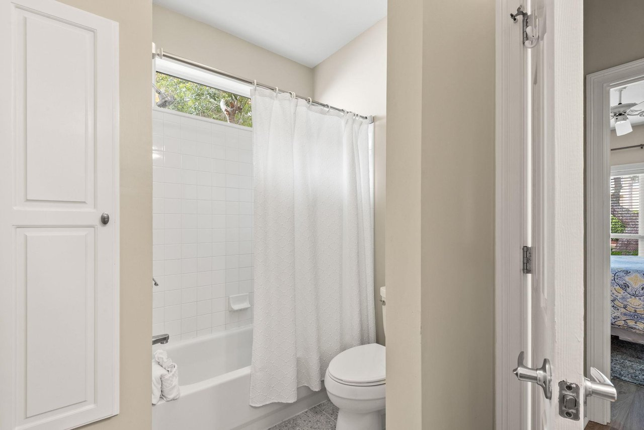 The bathroom features a refreshing showertub combo with crisp white tiling, soft natural light from above.
