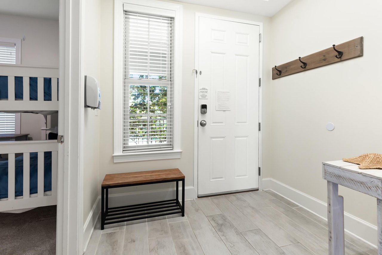 A bright entryway greets you with coastal charm—wooden hooks for beach bags, a bench for sandy feet, and glimpses of a cozy bunk room ready for family fun.