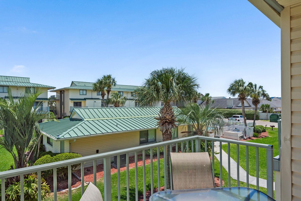 The property sits within a peaceful coastal community, surrounded by lush palm trees and neighboring properties with distinctive green roofs under bright blue skies.