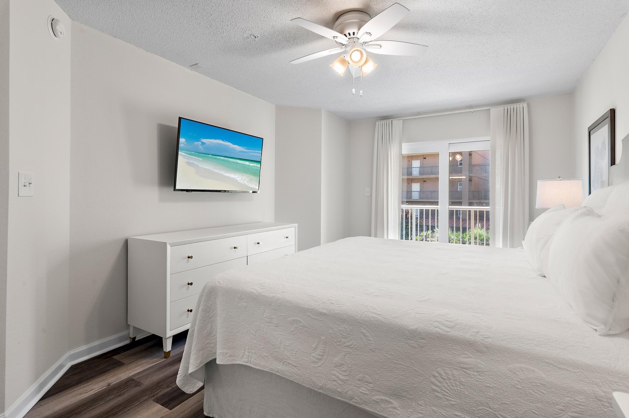 Step into your serene retreat with crisp white linens and gentle breezes from the balcony door.