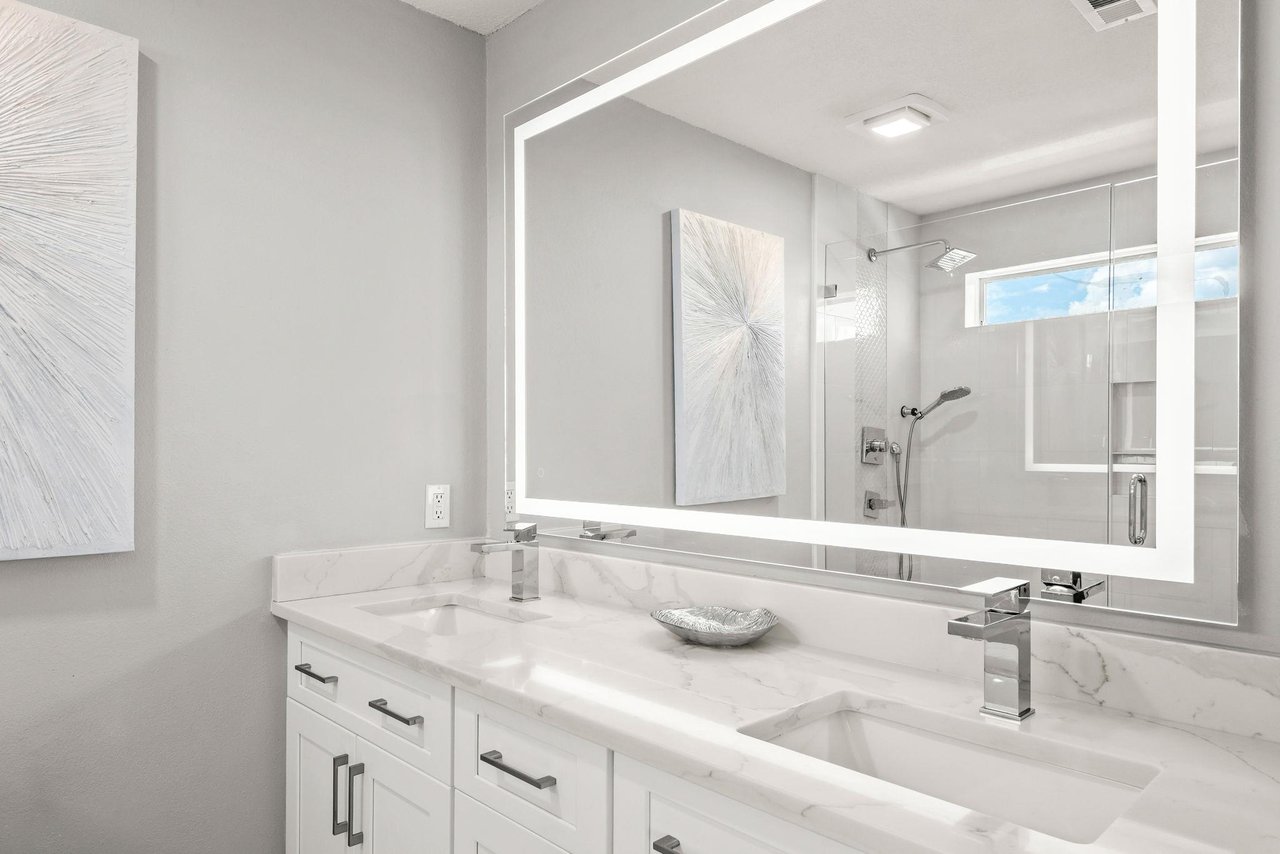 Bathroom 1 with dual sinks set in beautiful marble countertops, a bright LED mirror, and a sleek glassenclosed shower.