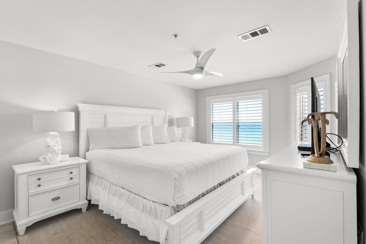 Drift off in this serene coastal bedroom with crisp linens, gentle sea breezes from the ceiling fan, and peaceful ocean glimpses through plantation shutters.