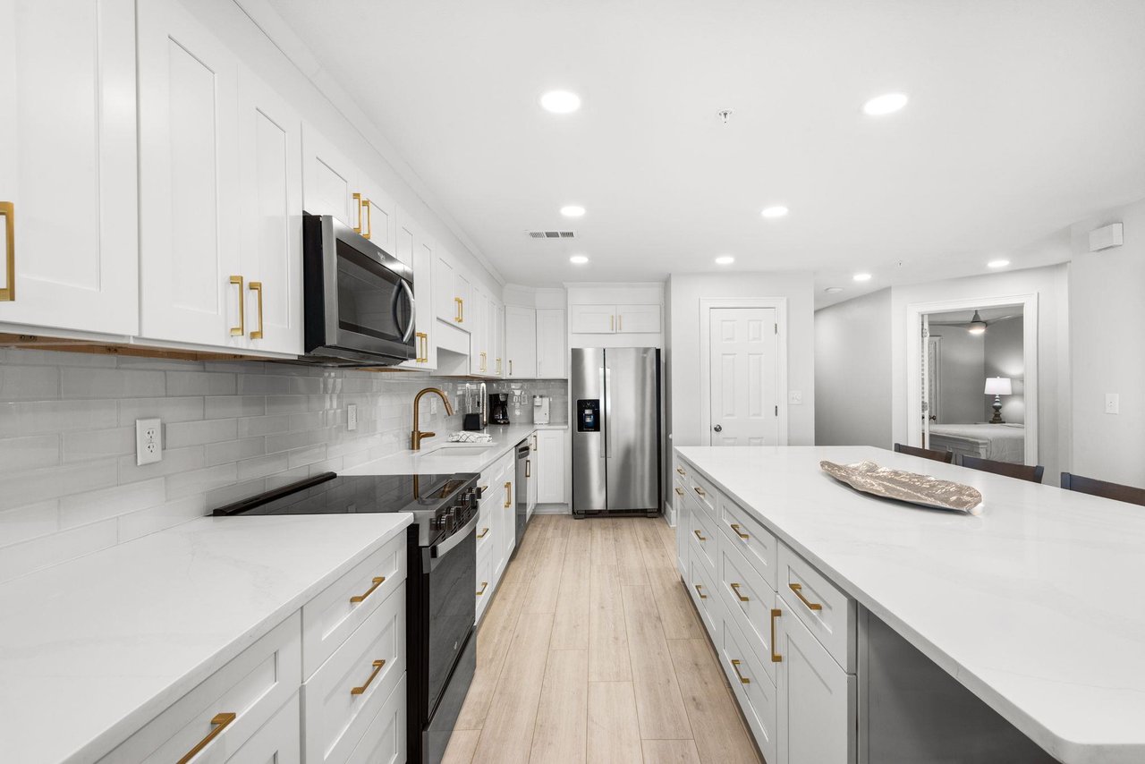 Your bright, fullyequipped kitchen awaits with sleek white cabinetry, gleaming countertops, and goldaccent hardware—perfect for preparing meals in style.