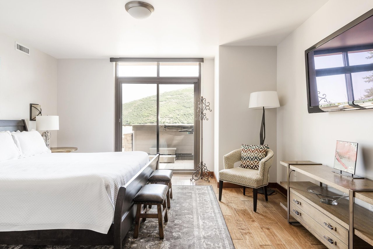 Main bedroom large flat screen wall mounted TV, accent armchair, and sliding glass doors for private deck access