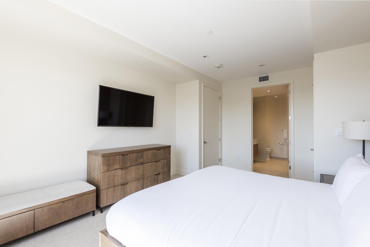 Spacious main bedroom suite with king bed, wooden dressers and woodsuede bench with wall mounted flat screen TV