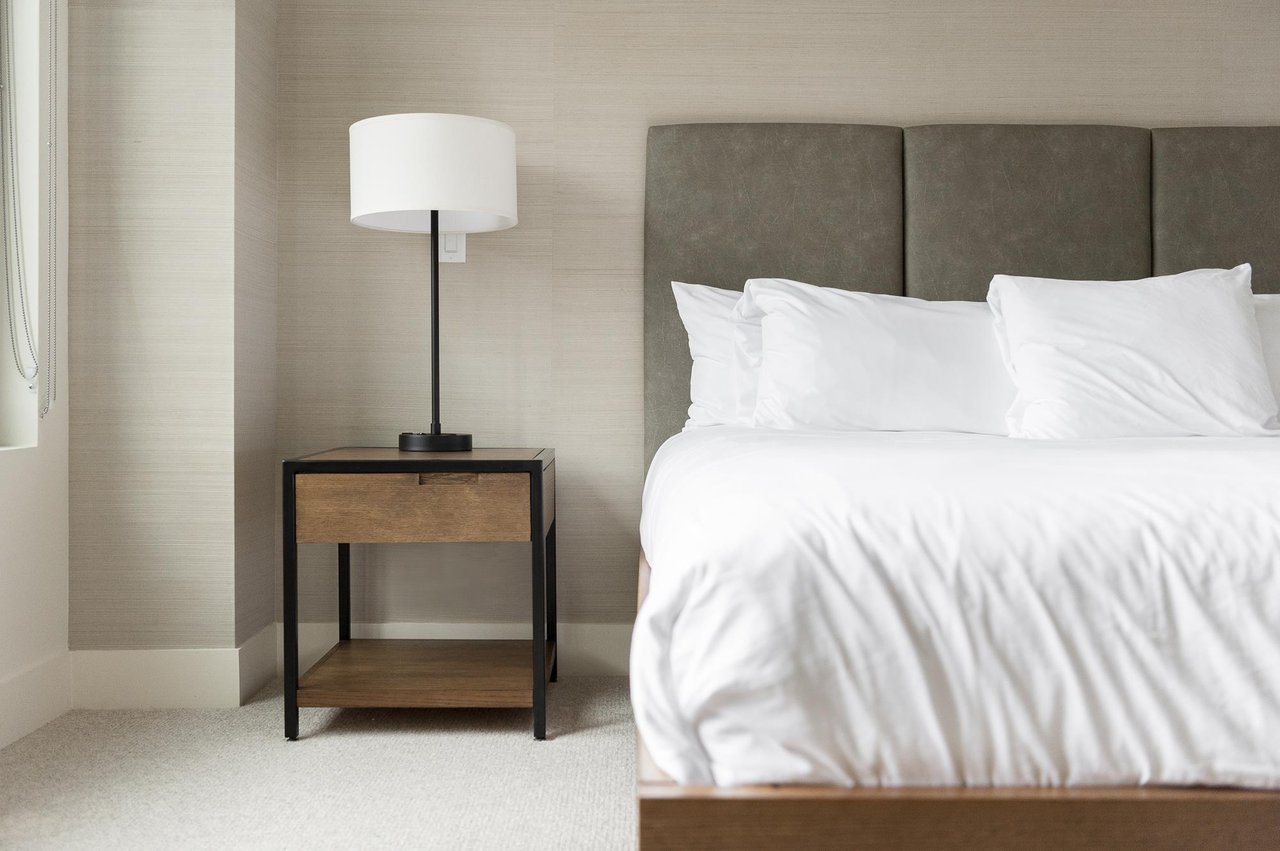Wood and metal storage nightstand with tall bedside lamp, suede tufted headboard at the king bed