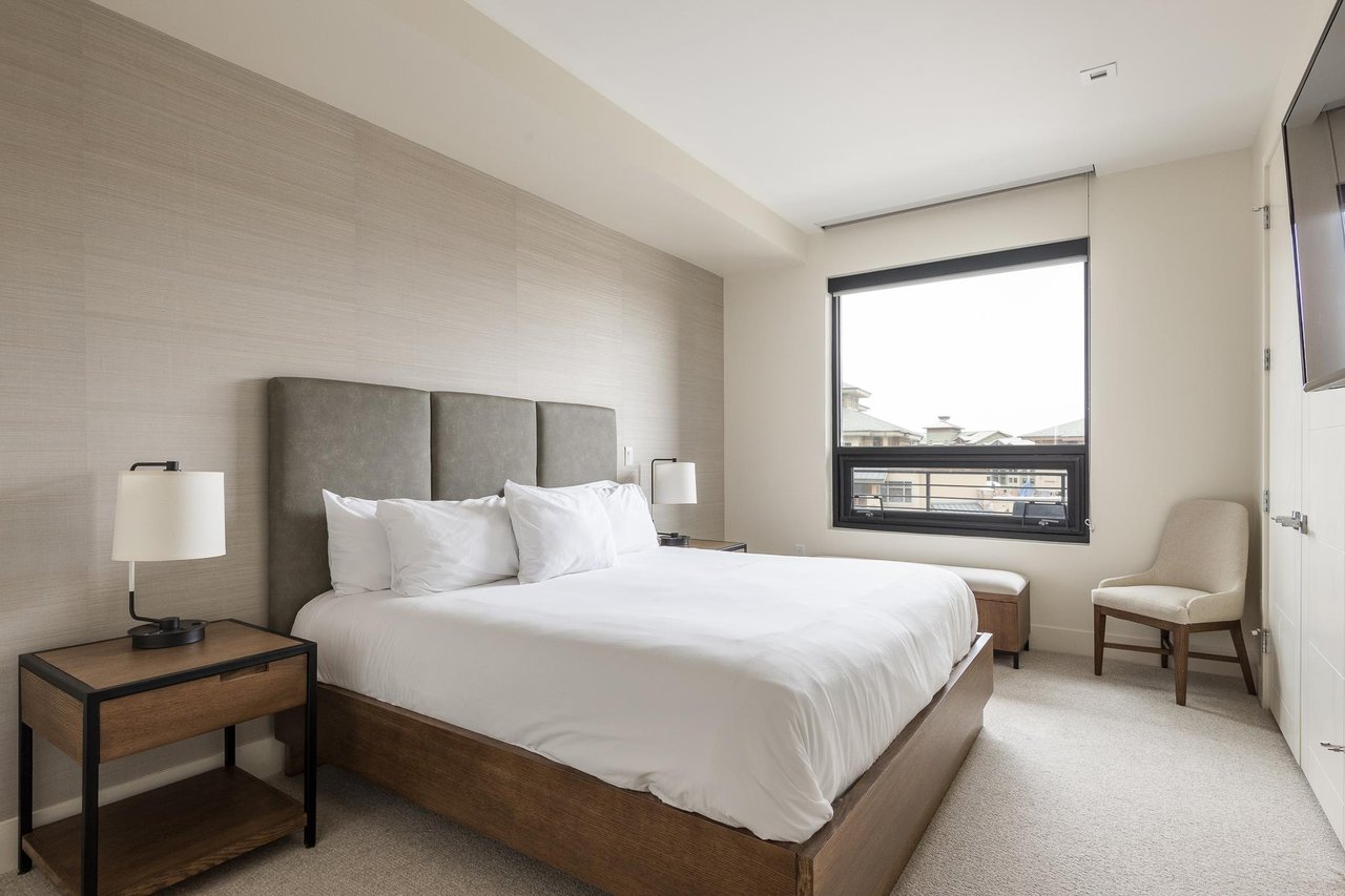 Guest bedroom with king bed, picture window, wooden bedside table and accent chair