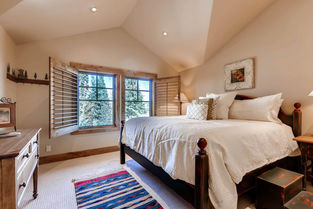 Graceful king bed in the third guest bedroom, wooden bedframe and large picture windows with wooden blinds