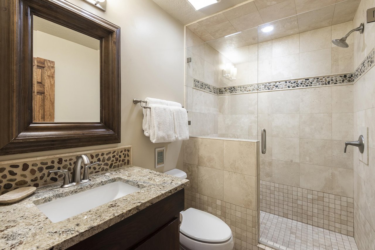 34 bathroom with tiled shower walls, glass shower door and river stone accent tiling, granite bathroom countertop, single vanity