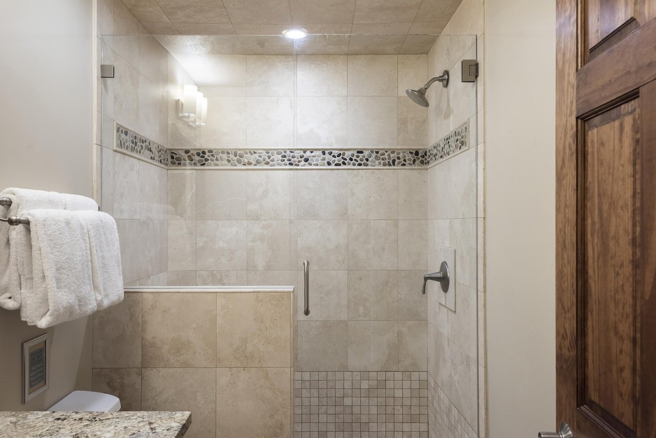 Spacious shower with chrome finishes, tiled shower walls with glass panel door