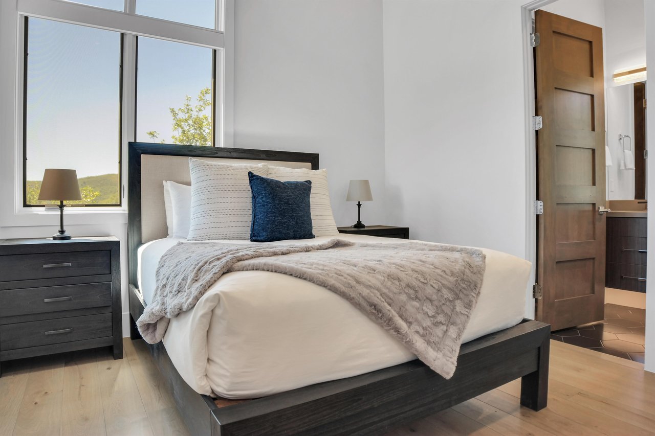 Vacation rental bedroom with a queen size bed and tall windows and solid wood furniture.