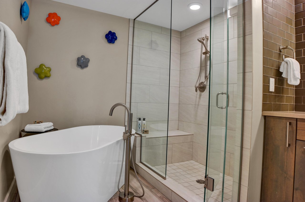 Standalone soaker tub and walkin shower with colorful ceramic flower art on the wall.