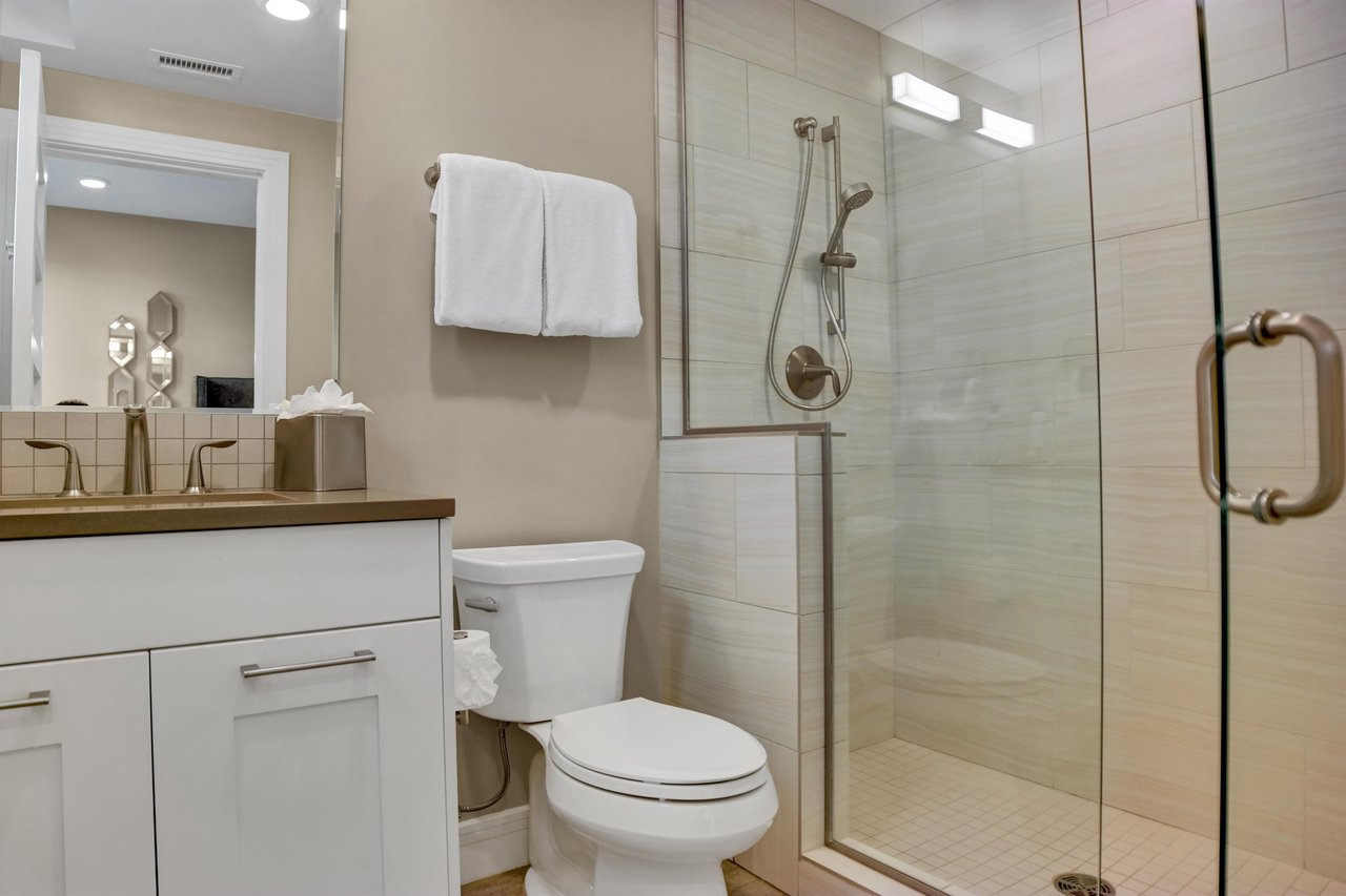 The ensuite bathroom with cream colored tiled shower with glass surround, white vanity with grey counter and toilet.