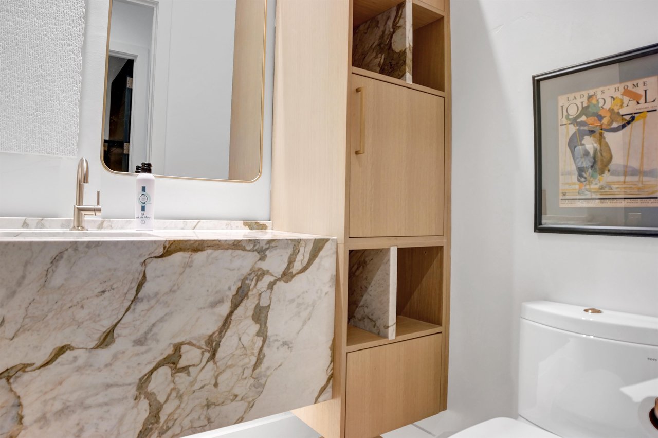 Half bathroom on the main level with a beautiful quartz sink basin, large mirror, and lightcolored wood builtin cabinets.
