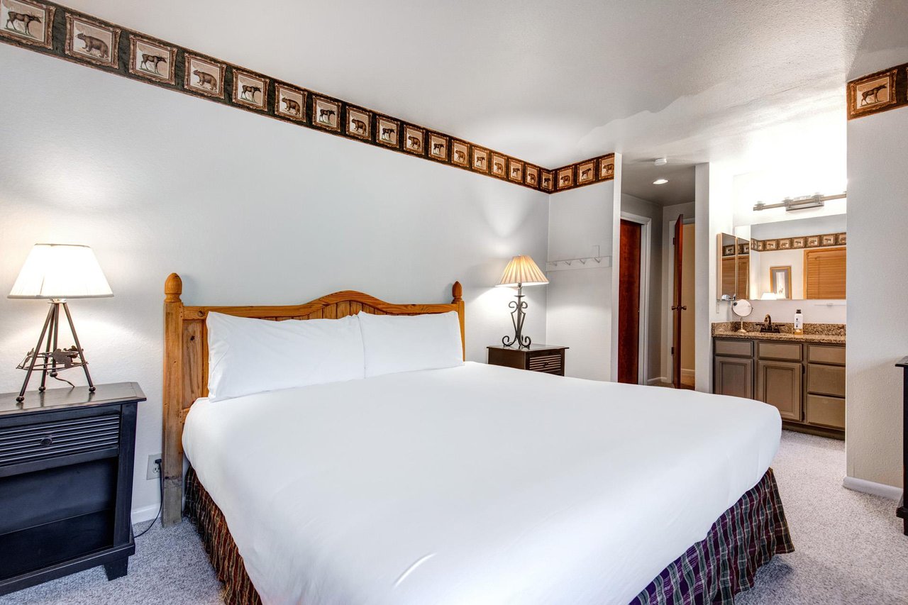 Snow Flowers main suite has a king size bed with white linens, 2 end tables and lamps and attached bathroom.