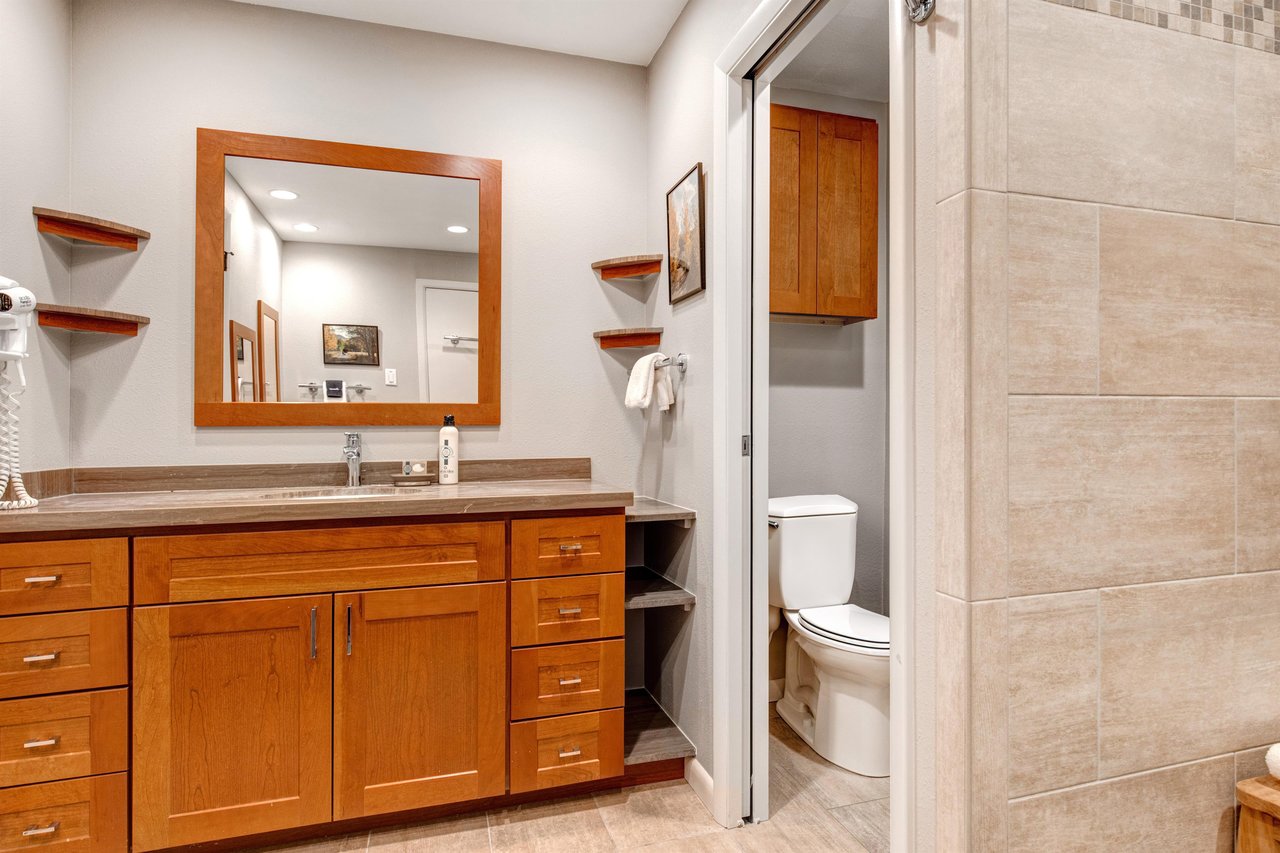 A wooden vanity with one sink vanity, large mirror and a door leading to a separate room for the toilet and shower.