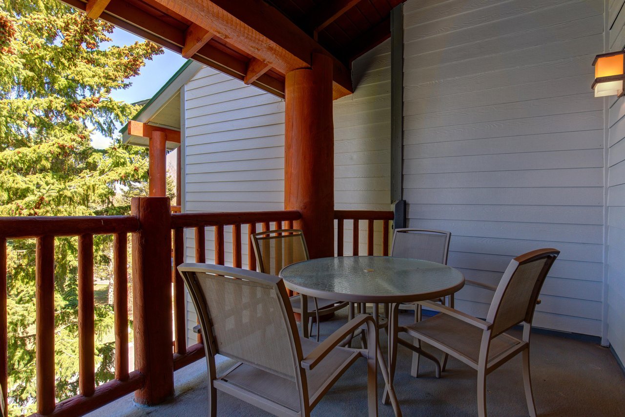Snow Flower 29s deck with wooden railing, round table with 4 chairs, and evergreen trees and blue sky beyond.