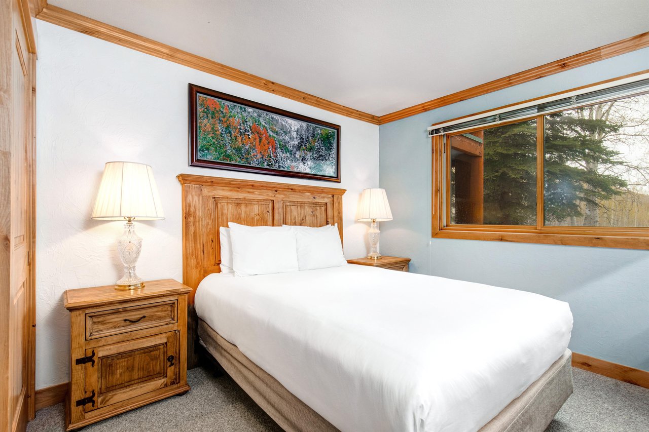 Snow Flower 43s second bedroom has a queensized bed, large wood headboard, white linens, and 2 end tables with lamps.