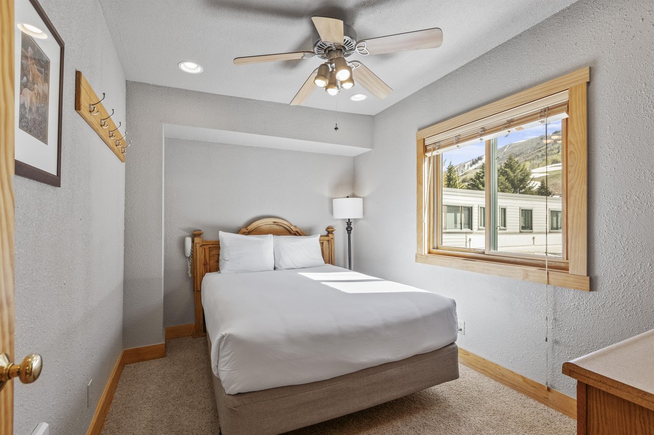 Snow Flower 72s bedroom with a queen bed, white sheets and pillows, greige walls and blonde wood accents.