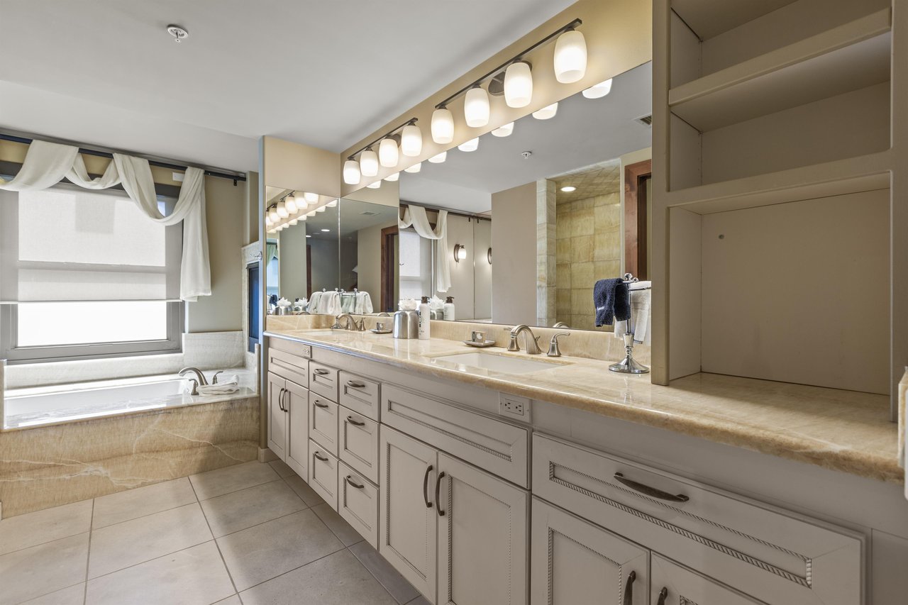 The second bedrooms en suite bathroom has a large two sink vanity, mirror, and lighting.