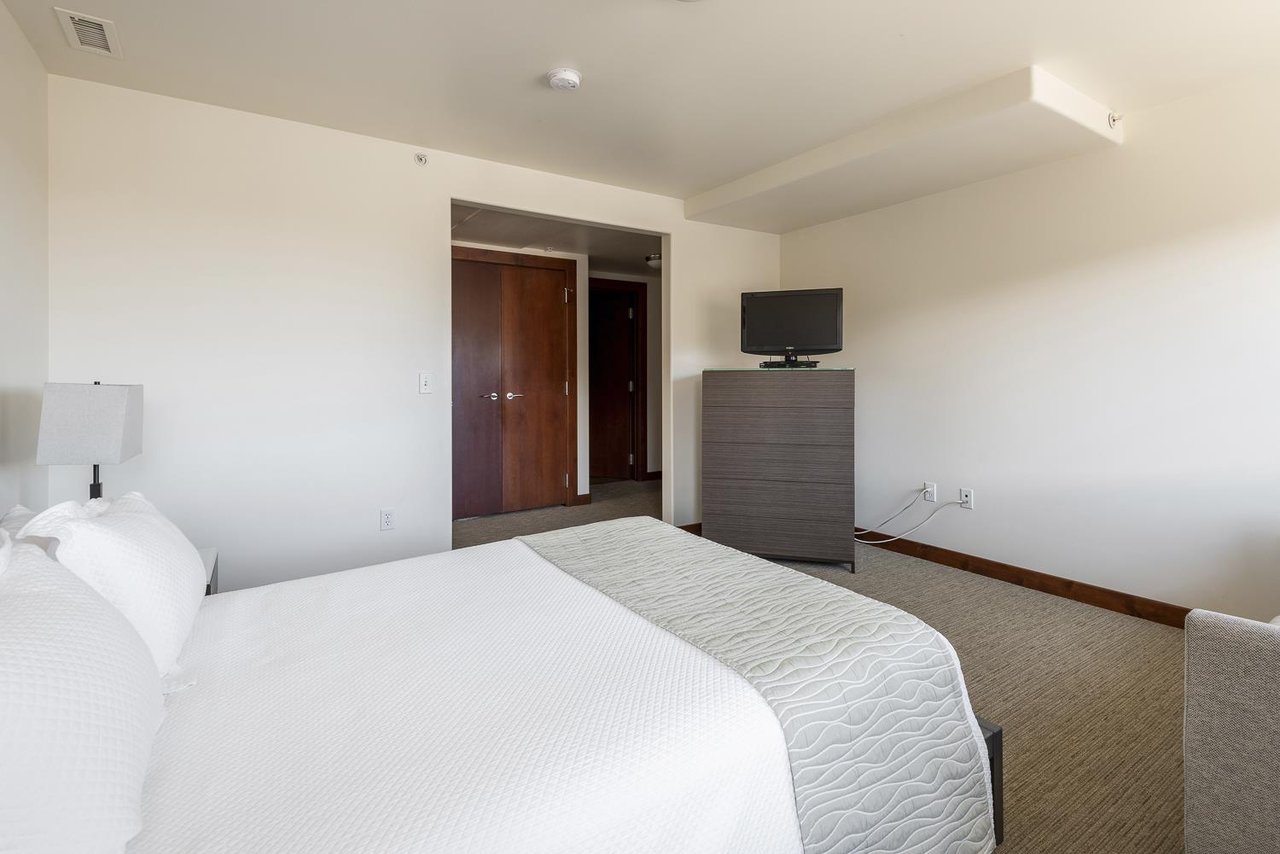 Guest queen bedroom with tall wooden dresser and flat screen TV