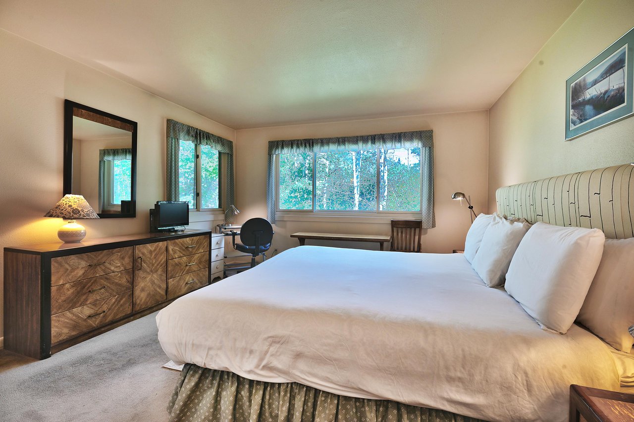 Main bedroom with wooden dresser, TV, and work desk in the corner under the picture window