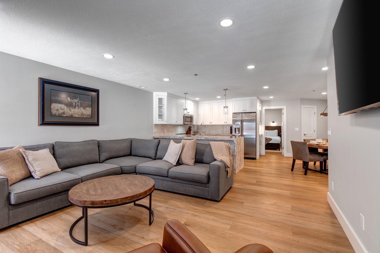 A spacious living room with warm tones furniture and blonde wood floors throughout.