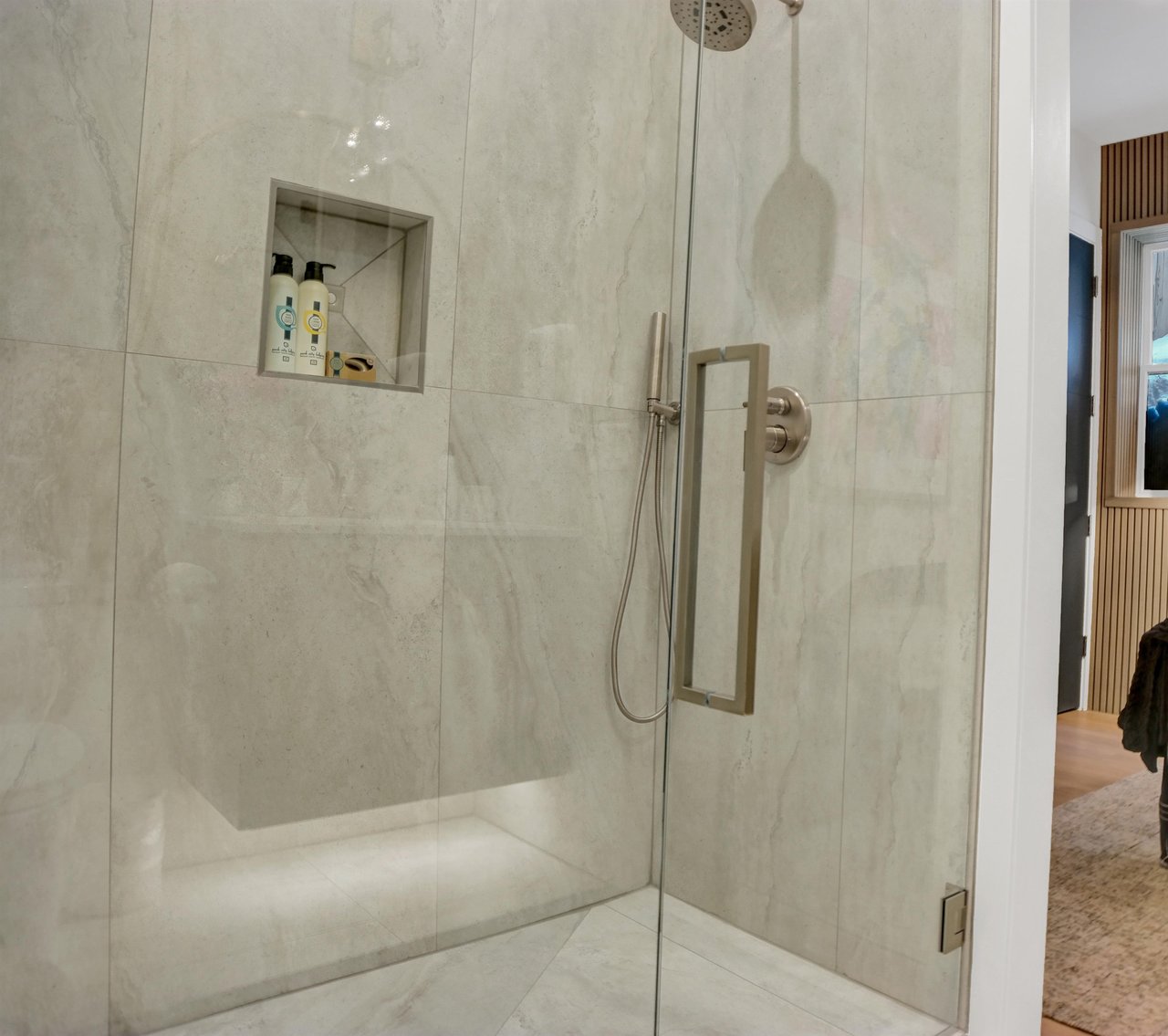 Walk in shower with light grey tile walls and floor and glass shower doors.