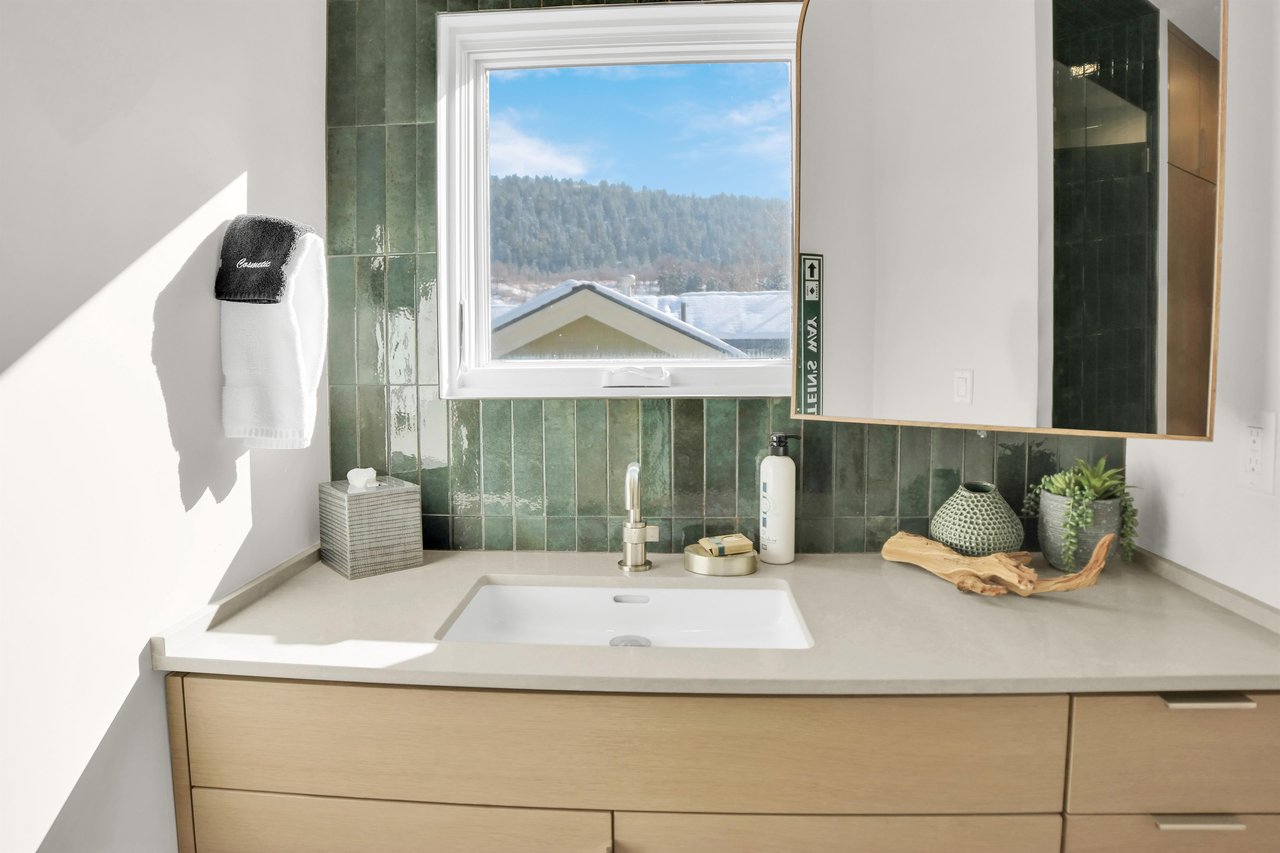 The bathroom has a wood vanity with deep green tile backsplash, window overlooking the mountain and town and large mirror.