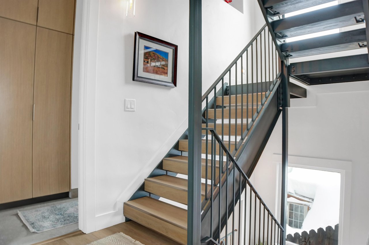 Open staircase for this 4 story home has light wooden treads and black iron railings and frame.