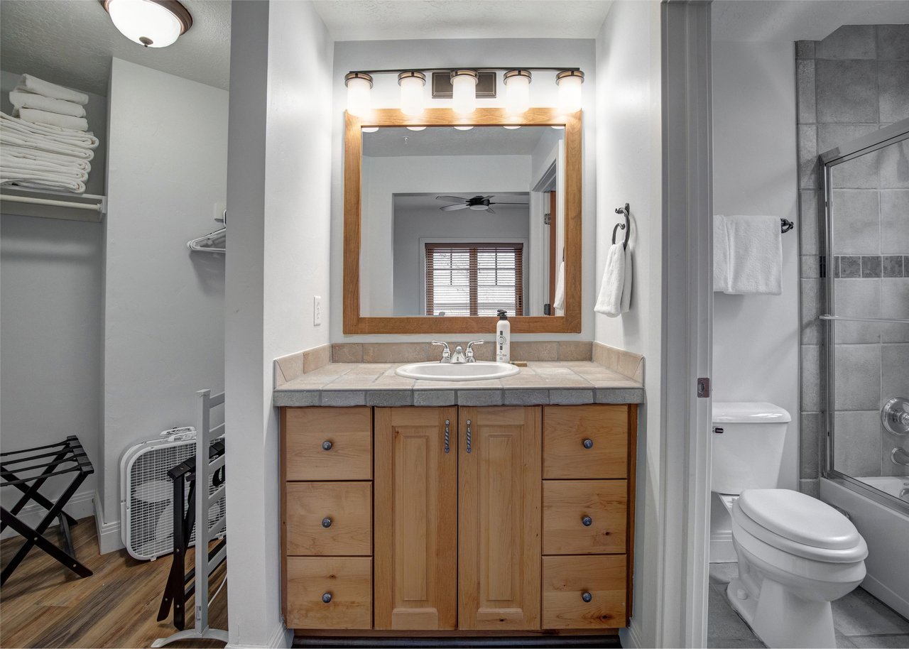 Step into your private bathroom featuring a warm wood vanity with stone countertops, welllit mirror, and separate shower area.