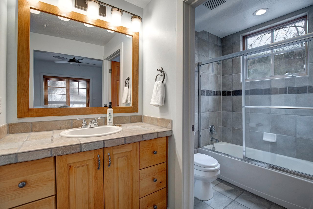 Relax in your private bathroom featuring elegant tile work, a spacious tubshower combo, and warm wood vanity.
