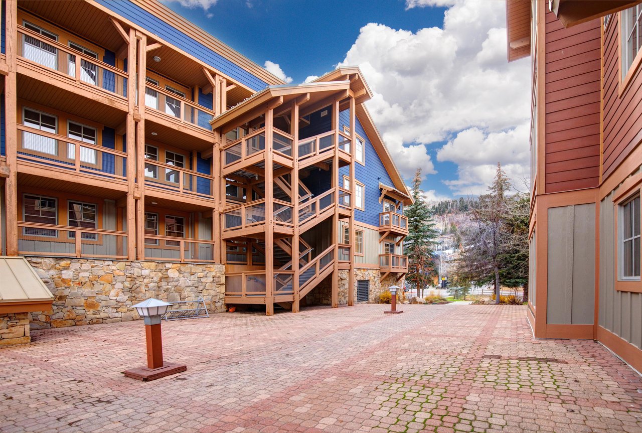 Modern multistory property buildings featuring wood and stone construction with spacious paved courtyard areas for guest access.