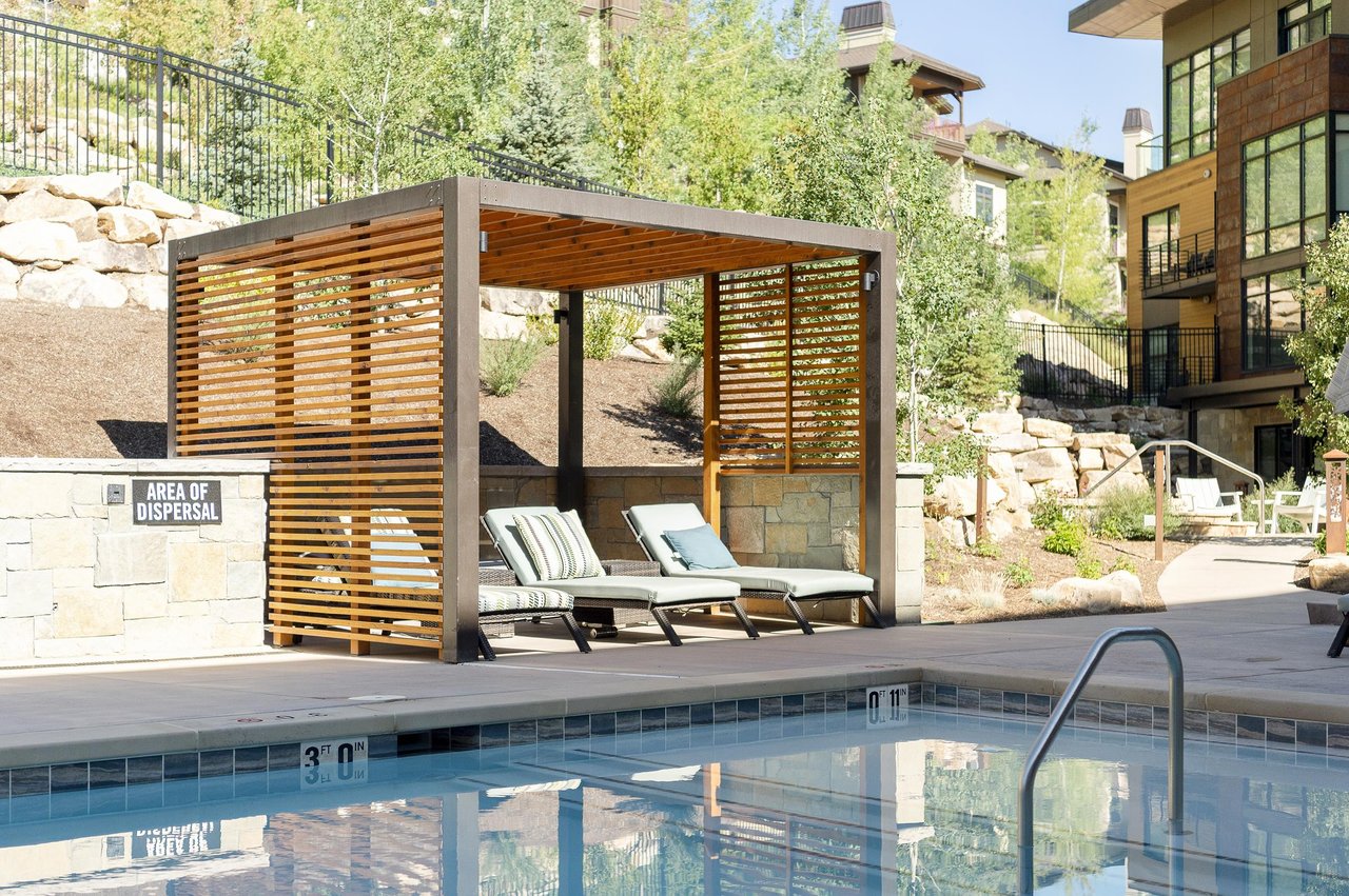 Poolside relaxation at the Lift Condominiums, three lounge chairs in the shade structure alongside the pool.