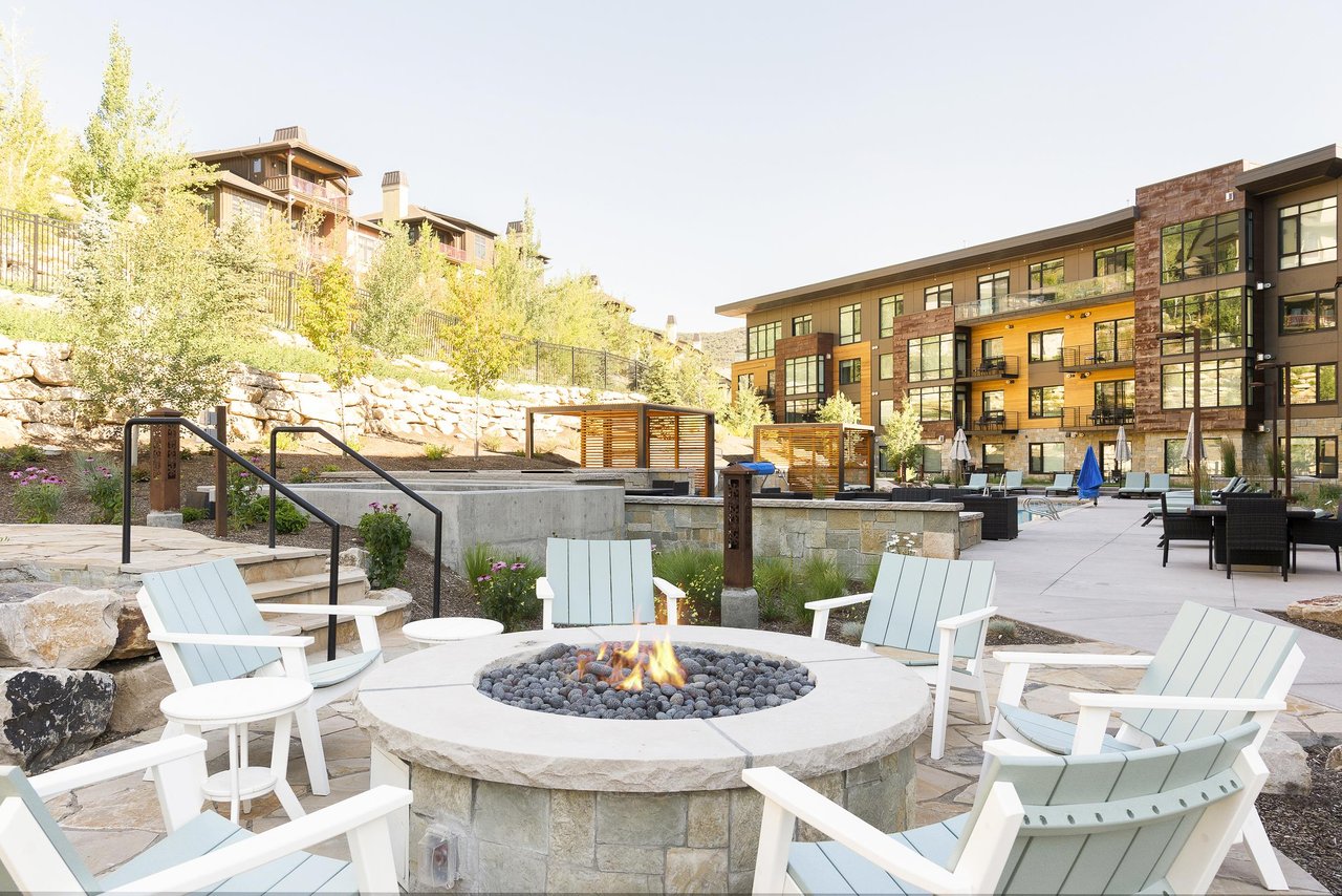 The Lift Condominiums outdoor circular firepit with white wooden Adirondack chairs, perfect for apres ski relaxation.